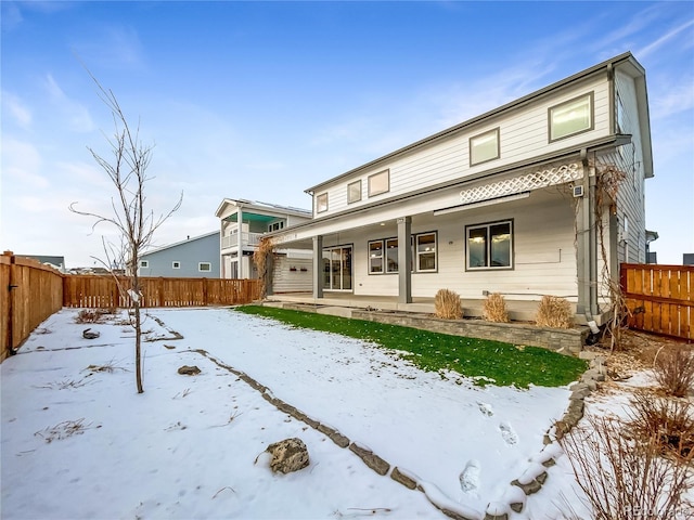 snow covered rear of property with a porch and a fenced backyard