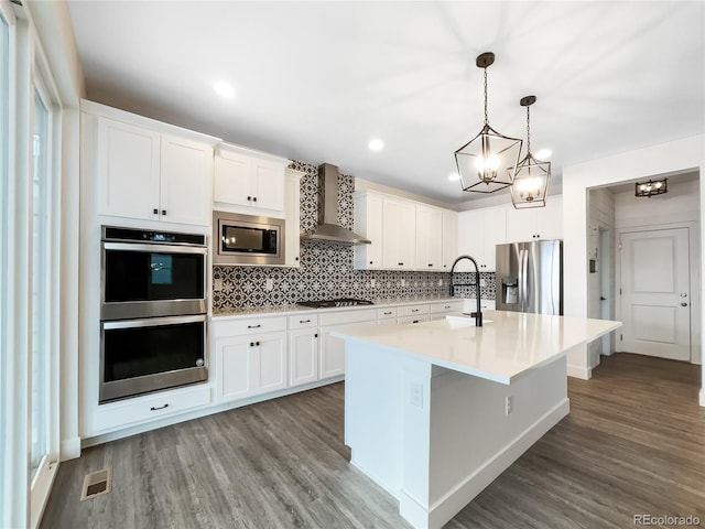 kitchen featuring stainless steel appliances, wall chimney range hood, light countertops, and white cabinetry