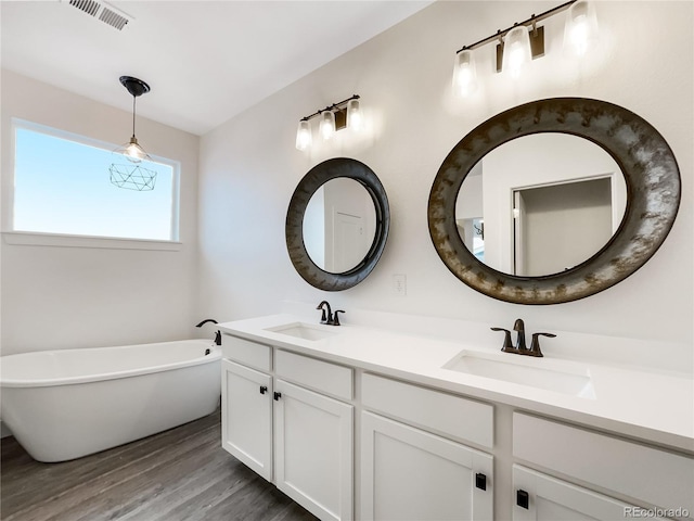 full bath featuring wood finished floors, a soaking tub, a sink, and visible vents