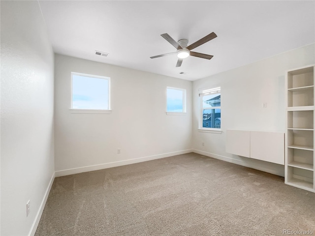 empty room featuring a ceiling fan, visible vents, light carpet, and baseboards