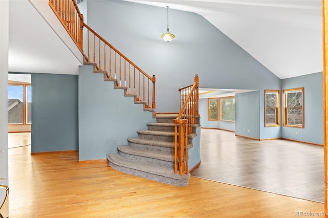 staircase featuring baseboards, high vaulted ceiling, plenty of natural light, and wood finished floors