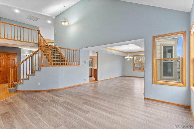 unfurnished living room with a notable chandelier, stairs, baseboards, wood finished floors, and visible vents