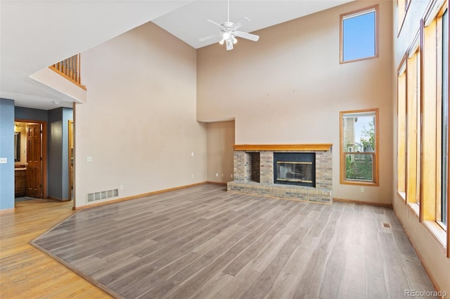unfurnished living room with a towering ceiling, ceiling fan, wood finished floors, and visible vents