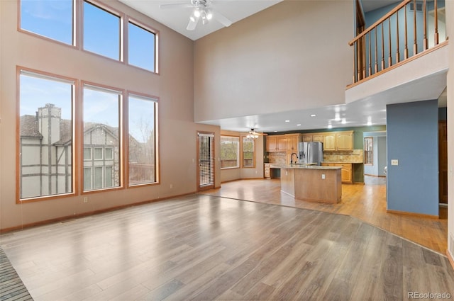 unfurnished living room featuring baseboards, a high ceiling, a ceiling fan, and light wood-style flooring
