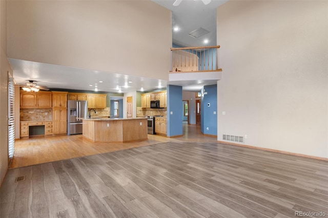 unfurnished living room with light wood-style floors, ceiling fan, a high ceiling, and visible vents