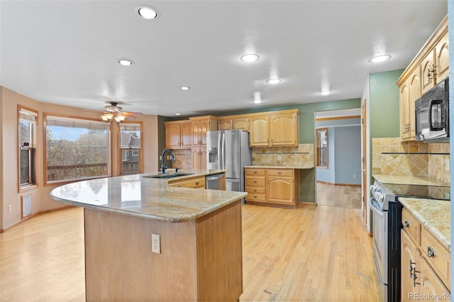 kitchen with ceiling fan, a center island with sink, a sink, light wood-style flooring, and appliances with stainless steel finishes
