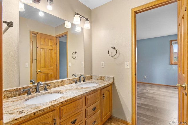 full bathroom featuring double vanity, baseboards, a sink, and wood finished floors