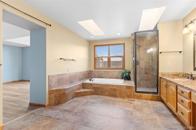 bathroom with a garden tub, vanity, baseboards, a stall shower, and a skylight