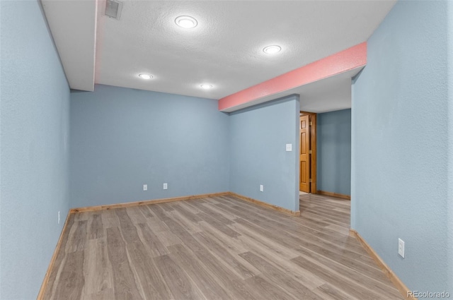 finished basement featuring visible vents, a textured ceiling, baseboards, and wood finished floors
