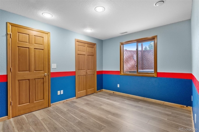 unfurnished bedroom featuring baseboards, visible vents, wood finished floors, and a closet