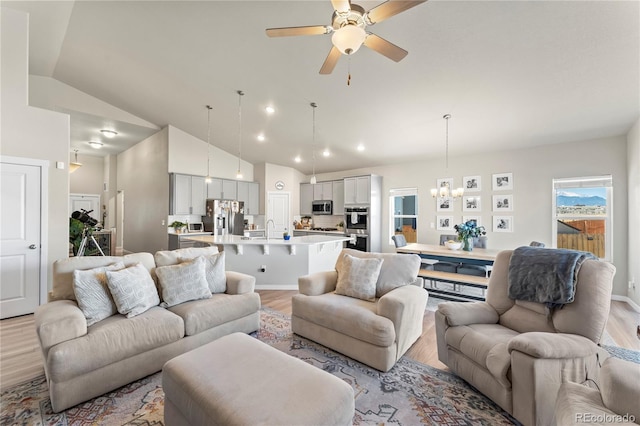 living room with high vaulted ceiling, recessed lighting, light wood-style flooring, and ceiling fan with notable chandelier