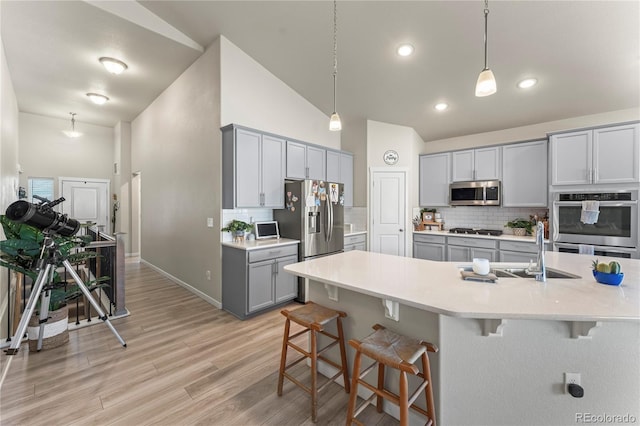 kitchen featuring a breakfast bar area, gray cabinetry, stainless steel appliances, a sink, and light countertops