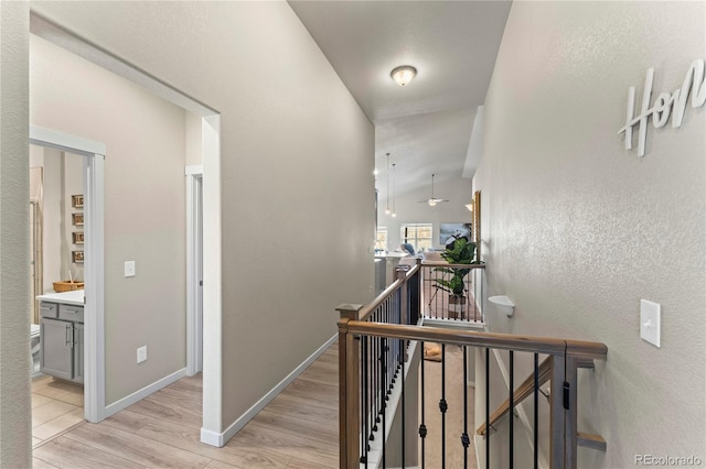 hallway with baseboards, an upstairs landing, and light wood-style floors