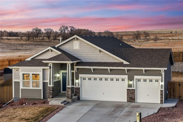 craftsman inspired home with roof with shingles, concrete driveway, an attached garage, fence, and stone siding