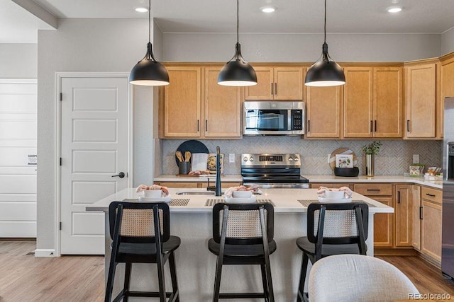 2118 Wagon Wheel Aly, Brighton, CO 80601 - kitchen with stainless steel appliances, light wood-style flooring, light countertops, decorative backsplash, and a kitchen island with sink