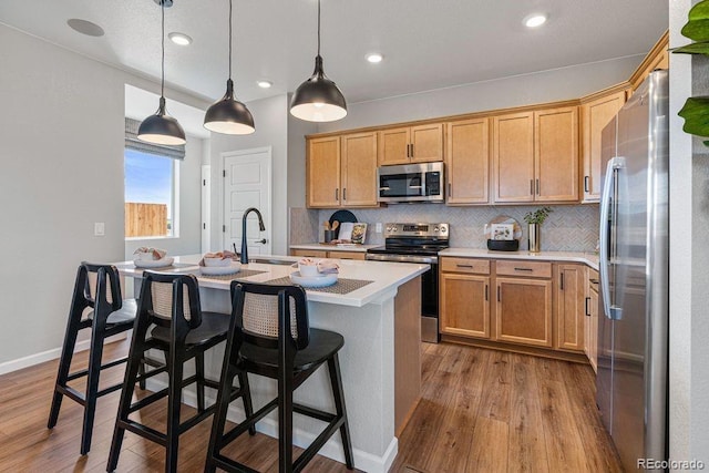 2118 Wagon Wheel Aly, Brighton, CO 80601 - kitchen featuring appliances with stainless steel finishes, a kitchen island with sink, wood finished floors, light countertops, and recessed lighting