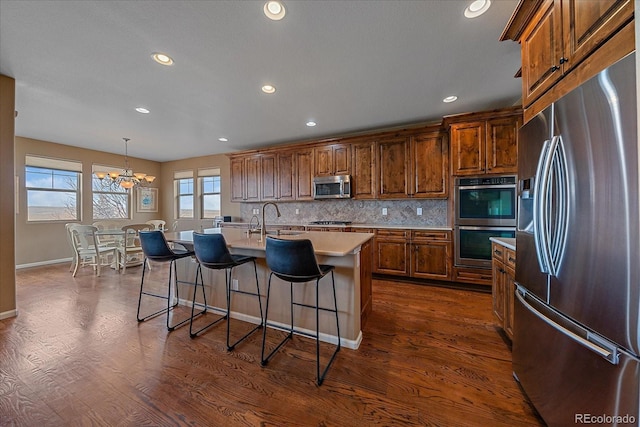 kitchen with pendant lighting, stainless steel appliances, dark hardwood / wood-style floors, tasteful backsplash, and an island with sink