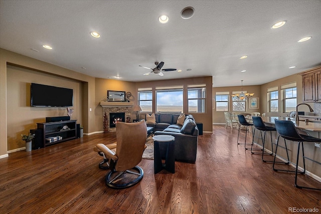 living room featuring a stone fireplace, ceiling fan with notable chandelier, dark hardwood / wood-style floors, and a textured ceiling