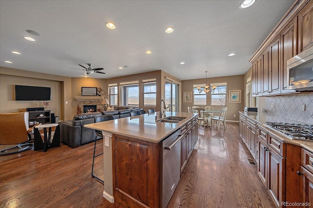 kitchen featuring a center island with sink, appliances with stainless steel finishes, dark wood-type flooring, open floor plan, and a sink