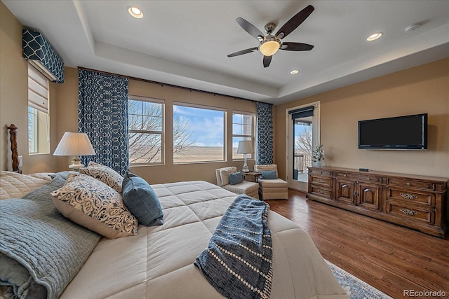 bedroom with ceiling fan, a tray ceiling, hardwood / wood-style floors, and access to exterior