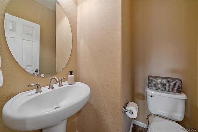 half bathroom featuring a textured wall, a sink, and toilet