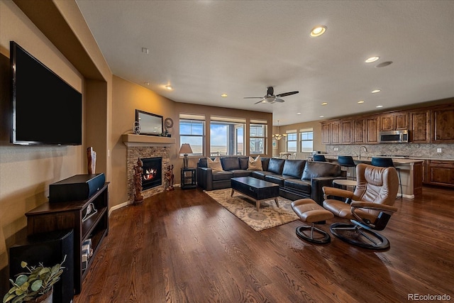 living room with ceiling fan, a stone fireplace, dark wood finished floors, and recessed lighting