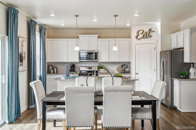 27756 E Byers Pl, Aurora, CO 80018 - kitchen featuring appliances with stainless steel finishes, a center island with sink, decorative backsplash, wood finished floors, and recessed lighting