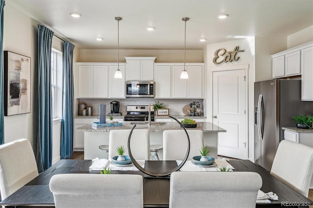 27756 E Byers Pl, Aurora, CO 80018 - kitchen with appliances with stainless steel finishes, an island with sink, backsplash, white cabinetry, and recessed lighting