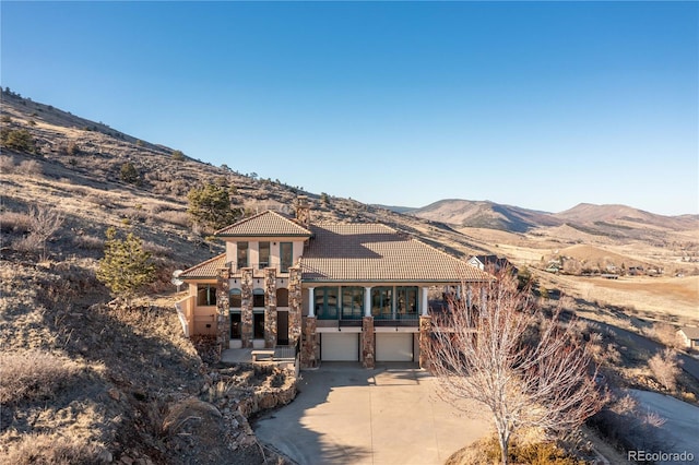 mediterranean / spanish-style house with an attached garage, a mountain view, a tiled roof, driveway, and stucco siding