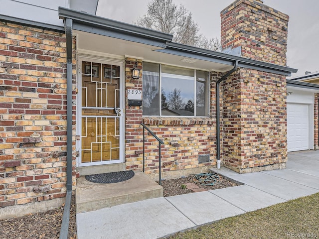 entrance to property featuring a garage, a chimney, and brick siding