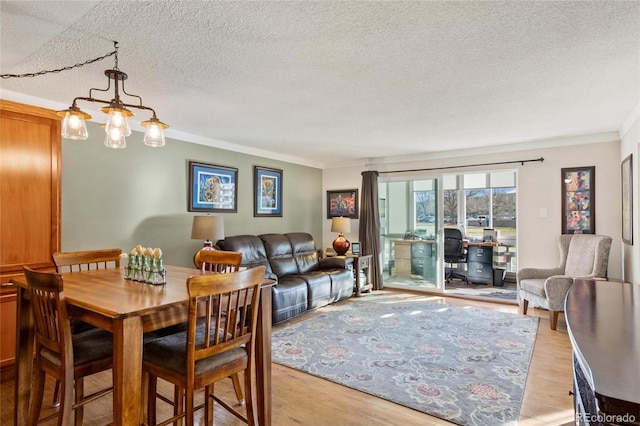 dining space featuring a textured ceiling, light wood-type flooring, an inviting chandelier, and ornamental molding