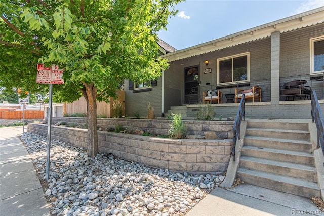 view of front of property with covered porch, brick siding, and fence