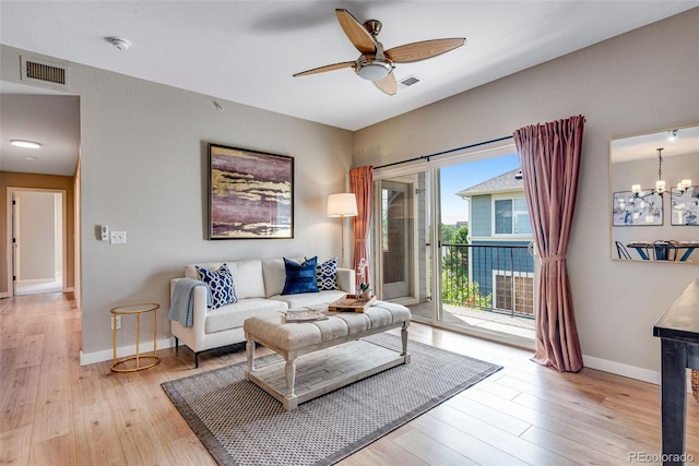 living room featuring ceiling fan with notable chandelier and light hardwood / wood-style flooring