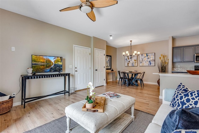 living room featuring ceiling fan with notable chandelier and light hardwood / wood-style floors