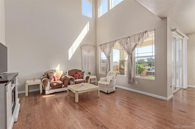 living room featuring light wood-type flooring, baseboards, and a towering ceiling