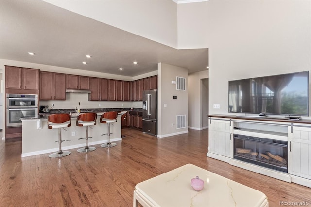 kitchen featuring wood finished floors, a kitchen bar, stainless steel appliances, visible vents, and under cabinet range hood