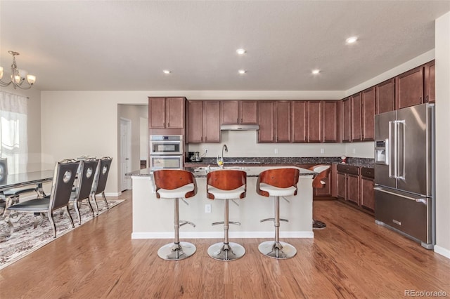 kitchen featuring under cabinet range hood, high end refrigerator, a center island with sink, and light wood-style floors