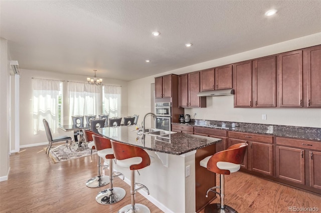 kitchen featuring a sink, stainless steel double oven, light wood-type flooring, a breakfast bar area, and under cabinet range hood
