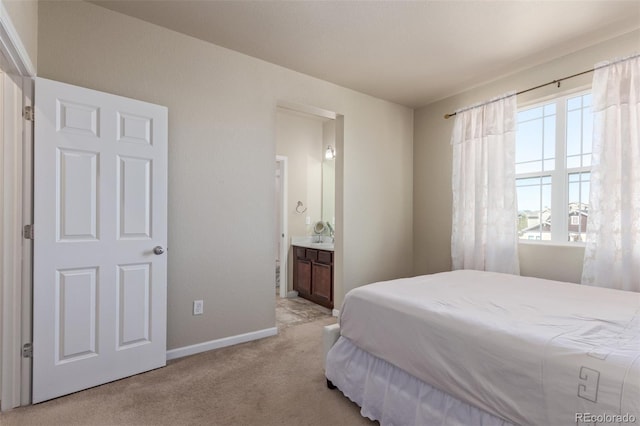 bedroom with ensuite bath, light carpet, and baseboards