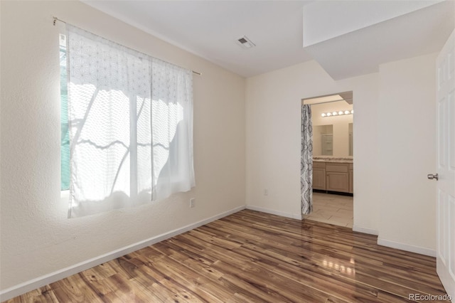 unfurnished bedroom featuring ensuite bath, baseboards, light wood-type flooring, and visible vents