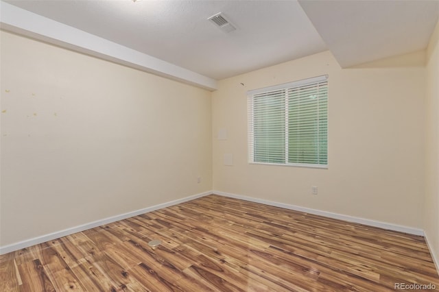spare room with baseboards, visible vents, and wood finished floors