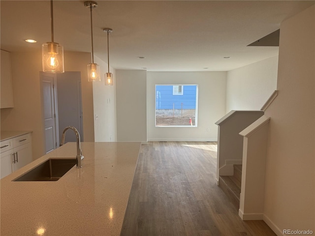 kitchen featuring decorative light fixtures, wood finished floors, open floor plan, a sink, and light stone countertops