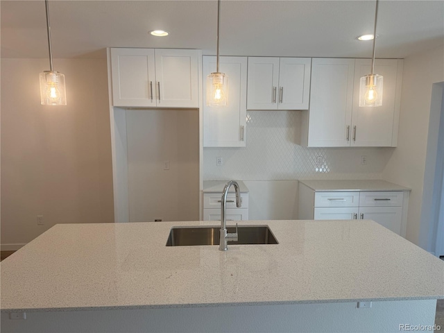 kitchen with light stone counters, a sink, white cabinets, tasteful backsplash, and pendant lighting