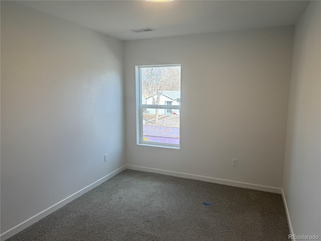 empty room featuring visible vents, dark carpet, and baseboards