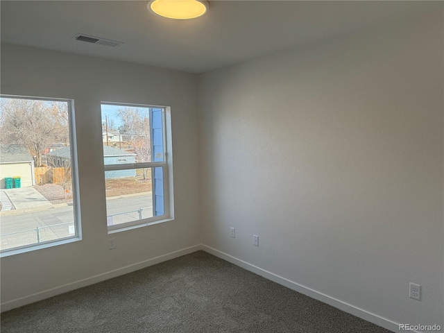 empty room featuring baseboards, visible vents, and dark carpet