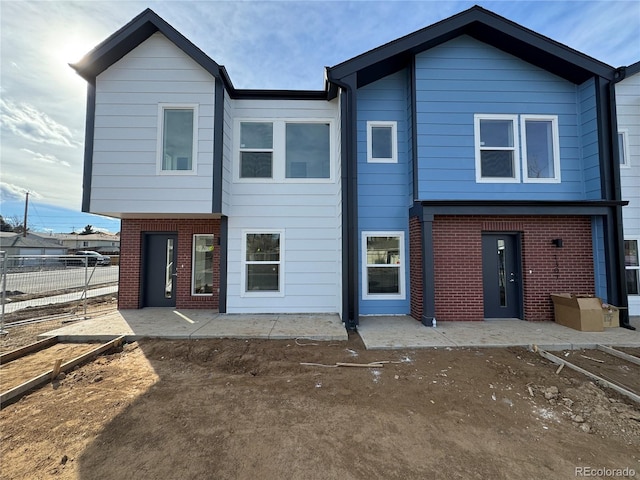 view of front of house featuring a patio, brick siding, and fence