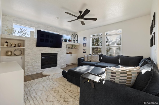 living room featuring hardwood / wood-style floors, a stone fireplace, a textured ceiling, and ceiling fan