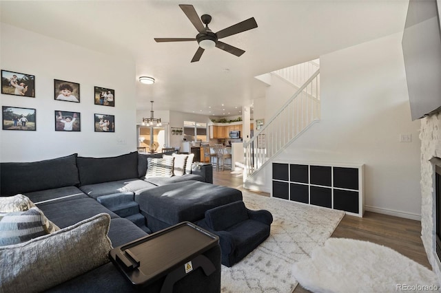 living room featuring a stone fireplace, ceiling fan with notable chandelier, and dark hardwood / wood-style floors