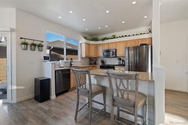 kitchen featuring black dishwasher, light stone counters, stainless steel fridge, and a kitchen bar