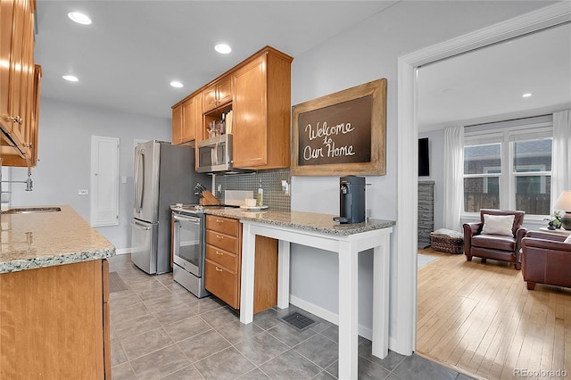 2212 Ingalls St, Edgewater, CO 80214 - kitchen with appliances with stainless steel finishes, brown cabinetry, tasteful backsplash, light stone countertops, and recessed lighting